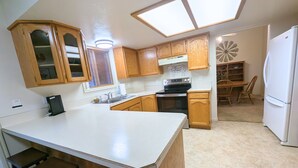A kitchen with wooden cabinets, a white countertop, a stove, and a refrigerator. - The Hideout-Single Level 2BR/2BA Townhouse near Highland! (Pocatello)