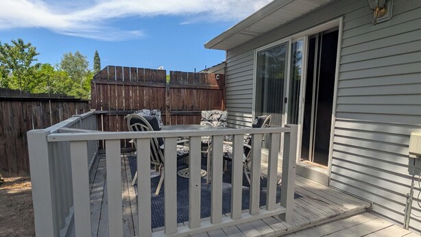 A covered patio with a white railing, a wooden deck, and a sliding glass door leading to a house. - The Hideout-Single Level 2BR/2BA Townhouse near Highland! (Pocatello)