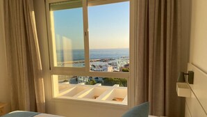 A hotel room with a large window offering a view of the sea and buildings. - Duplex penthouse facing the sea (Marbella)