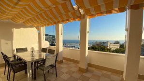 A balcony with a checkered floor, a table with chairs, and a striped awning. - Duplex penthouse facing the sea (Marbella)