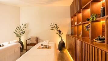 Relax in a serene spa room with two comfortable beds, a wooden reception desk, and a touch of greenery.