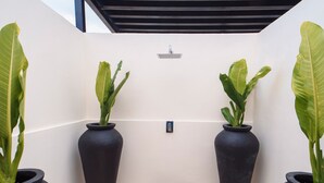 A modern outdoor area with a wooden deck, potted plants, and a white wall with a black roof structure.