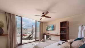 A modern hotel room with a large bed, a ceiling fan, a TV, and a balcony with outdoor seating.