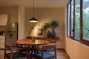 A modern kitchen with a dining area, featuring a wooden table, chairs, a hanging light, and large windows. - K'uyen Boutique Hotel (Tulum)