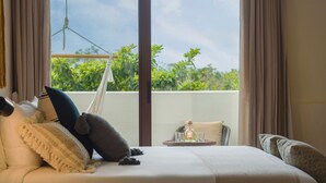 A hotel room with a bed, a small table with glasses and a bottle, and a view of greenery outside.