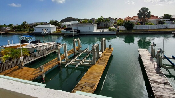 A marina with docked boats, a wooden pier, and residential buildings in the background. - North Finger Private Villa in Paradise (Jolly Harbour)