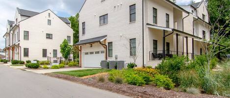 A modern two-story residential building with a garage, a covered porch, and a landscaped front yard.