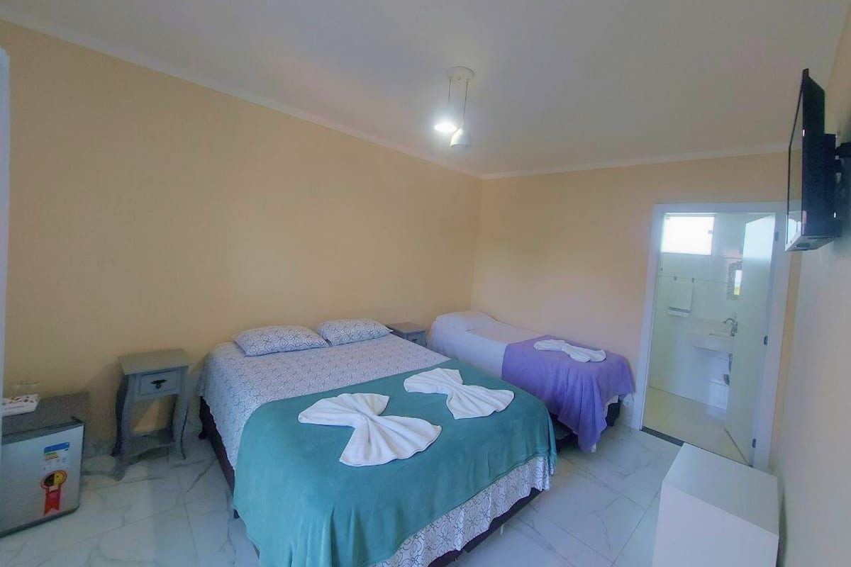 A hotel room with two beds, a small table, a nightstand, and a bathroom visible through an open door.