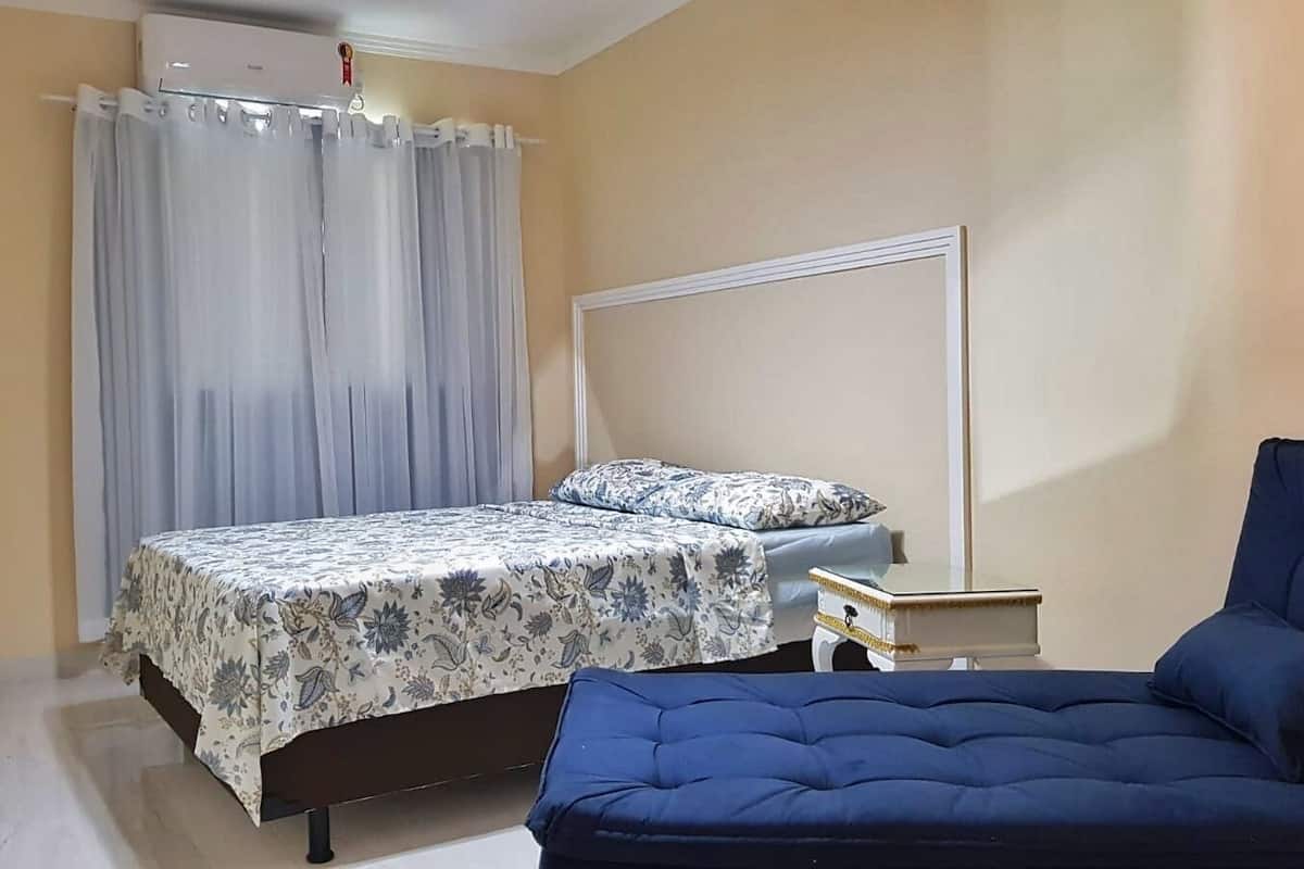 A bedroom with two beds, a nightstand, a chair, and a window with curtains.