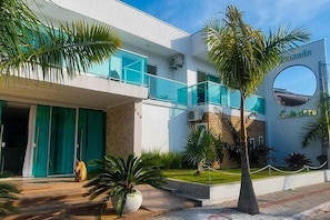 Un hotel moderno con fachada de vidrio, una ventana circular y un jardín cuidado con palmeras.