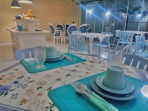 Comedor con mesas dispuestas para cuatro, con manteles florales y posavasos azules.