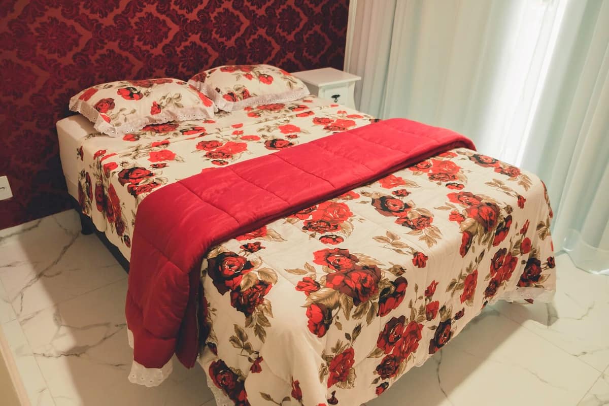 A double bed with floral bedding and a red blanket, a nightstand, and a red patterned wall.