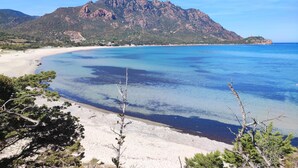 A coastal landscape with a mountain, clear blue waters, and sandy beach.