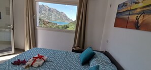 Une chambre avec un lit, une fenêtre donnant sur la montagne et un tableau accroché au mur.