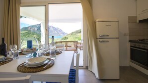 A dining area with a table set for two, a refrigerator, and a view of a mountainous landscape.