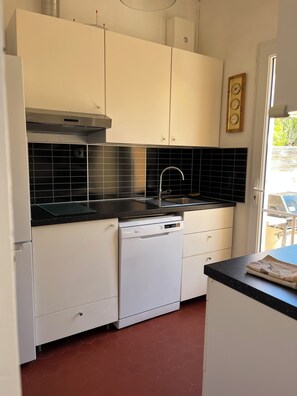 Una cocina con armarios blancos, encimera negra, lavavajillas y campana extractora de acero inoxidable.