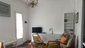 A living room with wicker furniture, a flat-screen TV, and a bookshelf. - Detached villa in residential area, beach and shops nearby (Sanary-sur-Mer)