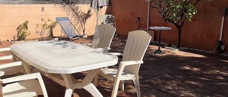 An outdoor patio with a round table and chairs, surrounded by a tiled floor and a wooden fence.