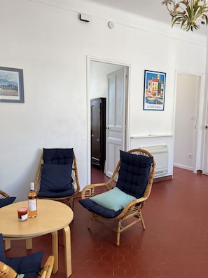 A room with wicker chairs, a round table, a bottle, a poster, and a radiator.