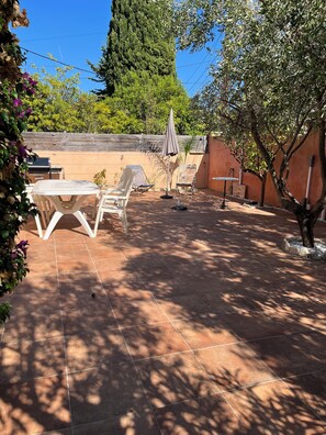 An outdoor patio with a table and chairs, surrounded by trees and a wooden wall.