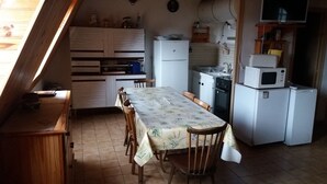 Une cuisine compacte comprenant une table à manger, des chaises en bois et les appareils électroménagers de base, comme un réfrigérateur, un four à micro-ondes et un four traditionnel.