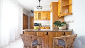 A kitchen with wooden cabinets, a central island with chairs, and a potted plant. - Home2Book Caletillas Breeze & Comfort (Tenerife)