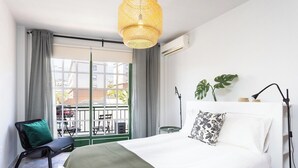 A bedroom with a large bed, a green chair, a balcony view, and a hanging light fixture. - Home2Book Caletillas Breeze & Comfort (Tenerife)