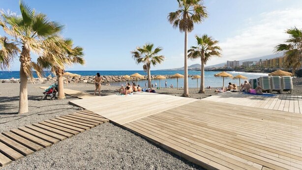 A beach with wooden walkways, palm trees, and umbrellas. - Home2Book Caletillas Breeze & Comfort (Tenerife)