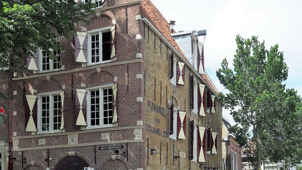 Un bâtiment historique à la façade en briques, doté de grandes fenêtres et d’une terrasse avec des parasols.