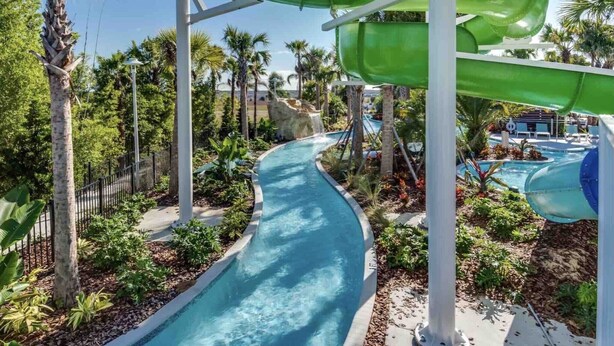 Un toboggan aquatique se terminant dans une piscine, entouré de palmiers et d’un espace piscine agrémenté de chaises longues.