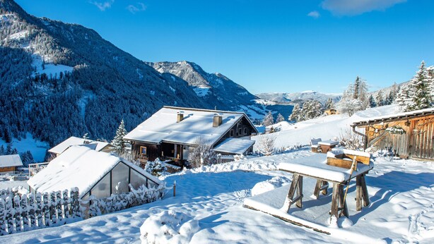 Un village enneigé, avec des bâtiments en bois, une clôture en bois et un ciel bleu dégagé.