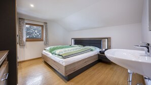 Une chambre à coucher avec un lit en bois, une table de chevet, un lavabo blanc et une fenêtre avec des rideaux.