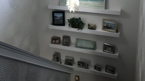 Eine Treppe mit einer Chandelüster, gerahmten Bildern und einer kleinen Pflanze auf Regalen.