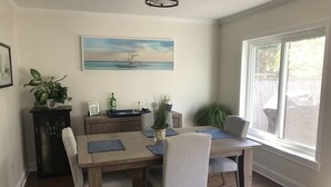 Ein Essbereich mit einem Holztisch, vier Stühlen, einem Seestück und einem Fenster mit Blick ins Freie.