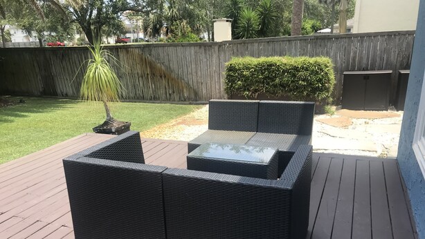 Eine Terrasse mit einem schwarzen Korbstuhl-Set und einer Holzkonstruktion, umgeben von einem Holzboden und einem Holzzaun.