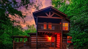 A two-story log cabin with a balcony, surrounded by dense forest. - Private, 1 mile to Downtown, Hot Tub, Firepit (Gatlinburg)