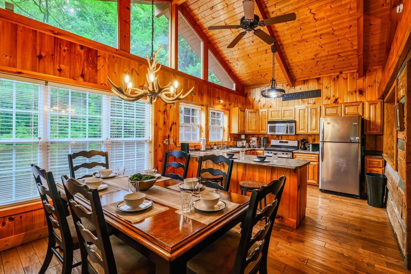 Une cabane en bois comprenant un coin repas, une cuisine et de grandes fenêtres.
