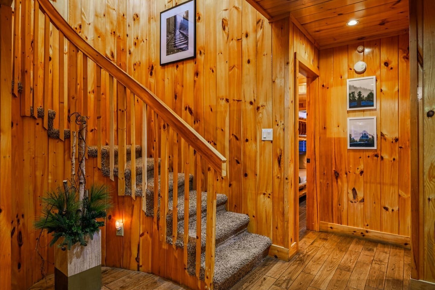 Un escalier en bois avec une rampe, une petite plante et des tableaux encadrés accrochés aux murs.