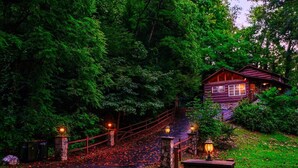A rustic cabin with a stone pathway leading to a wooden gate, surrounded by dense forest. - Private, 1 mile to Downtown, Hot Tub, Firepit (Gatlinburg)