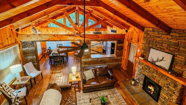 A spacious loft-style room with a high ceiling, wooden beams, a stone fireplace, and a dining area with a view of the kitchen. - Private, 1 mile to Downtown, Hot Tub, Firepit (Gatlinburg)