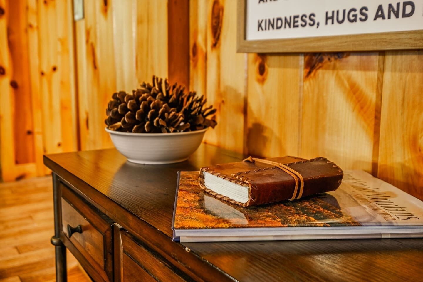 A wooden table with a bowl of pinecones and a book with a brown cover.