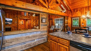 A rustic cabin interior with a wooden dining area, kitchen with granite countertop, and a cozy seating area with a fireplace. - Private, 1 mile to Downtown, Hot Tub, Firepit (Gatlinburg)