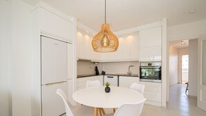 A modern kitchen with white cabinetry, a round dining table with chairs, and a hanging light fixture.
