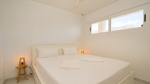 A bedroom with a large bed, two bedside tables, a window with a mountain view, and a small stool with a lamp.