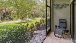 A room with a large glass door leading to a garden with trees and a pathway. - Gorgeous Ground Floor Condo in World Class Resort, Pool, Spa, Amenities Galore! (Naples)