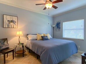 A bedroom with a bed, a nightstand, a lamp, a ceiling fan, and artwork on the walls. - Gorgeous Ground Floor Condo in World Class Resort, Pool, Spa, Amenities Galore! (Naples)