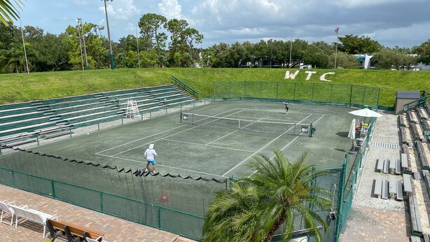 An outdoor tennis court with seating and a net. - Gorgeous Ground Floor Condo in World Class Resort, Pool, Spa, Amenities Galore! (Naples)