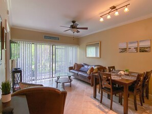 A dining area with a table and chairs, a ceiling fan, and a view of the outdoors through large windows.