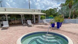 A circular pool with a tiled edge, surrounded by a brick patio. There are lounge chairs and a covered seating area with tables. - Gorgeous Ground Floor Condo in World Class Resort, Pool, Spa, Amenities Galore! (Naples)