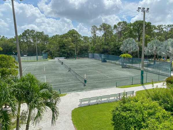 A tennis court surrounded by trees and a bench.